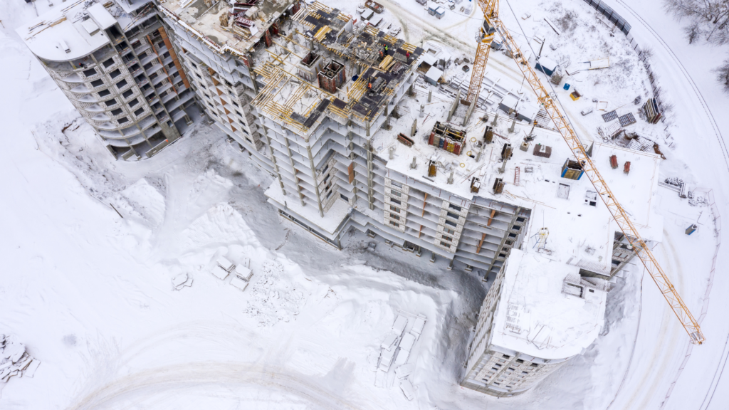 Image d'un chantier de construction paralysé par l'enneigement, illustrant la problématique du régime des Congés Intempéries dans le secteur du BTP. La neige recouvre les équipements et les structures, mettant en évidence l'impact des conditions météorologiques sur l'avancement des travaux. Cette situation démontre l'importance cruciale de la planification et de la gestion des congés intempéries dans l'industrie de la construction."